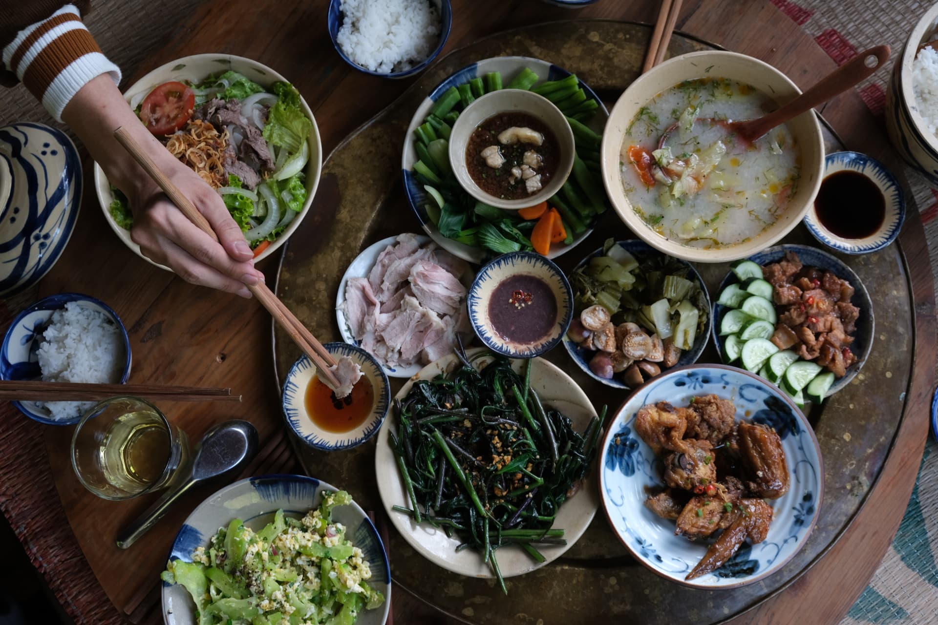 A Vietnamese dinner spread with herbs, bowls, and hands reaching with chopsticks