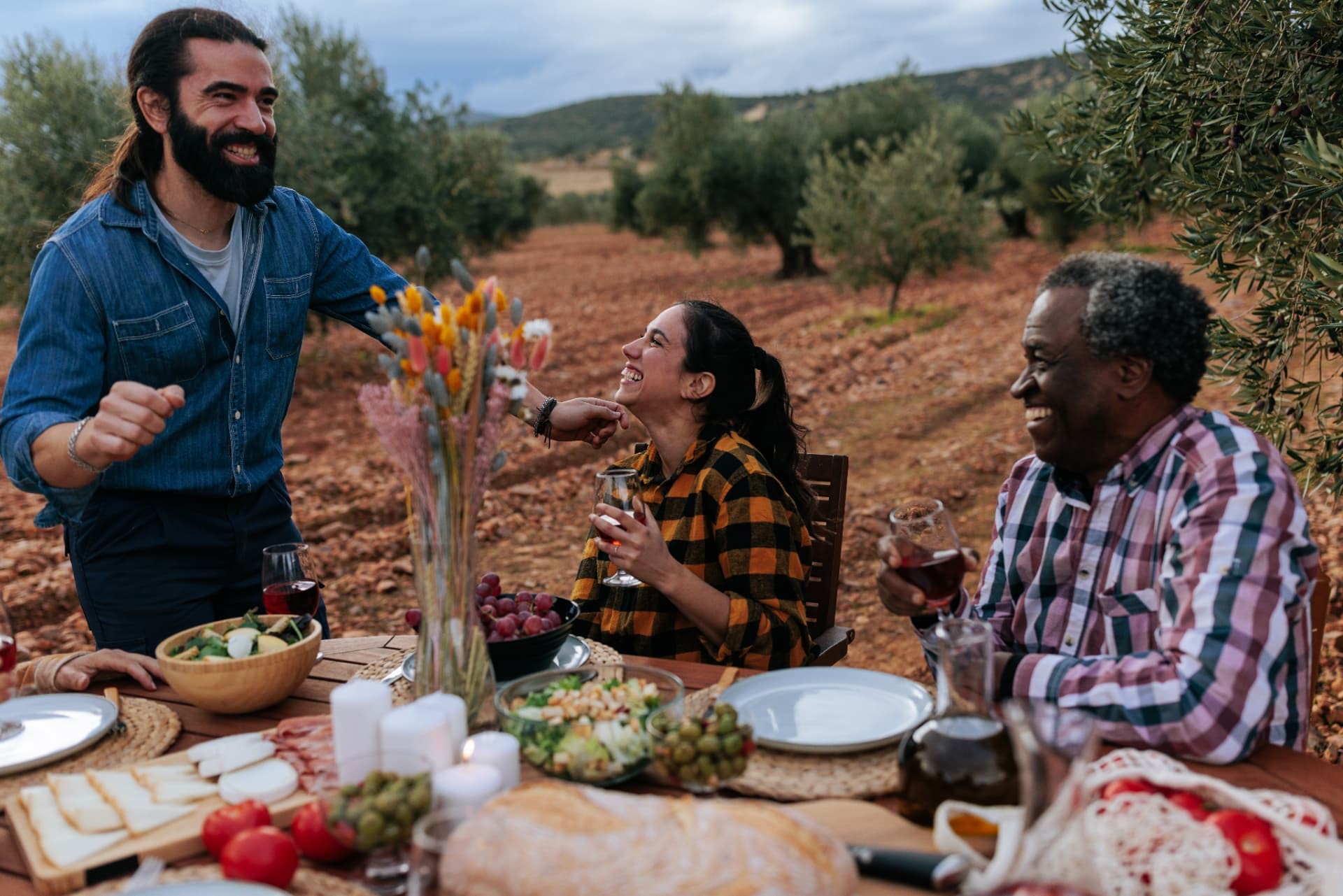 Friends gathering around a long table in an olive grove