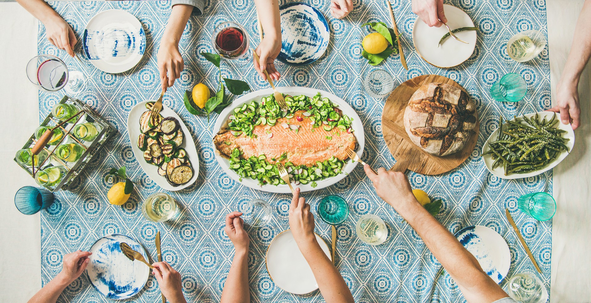 Friends sharing salmon, summer vegetables and bread on blue patterned linen