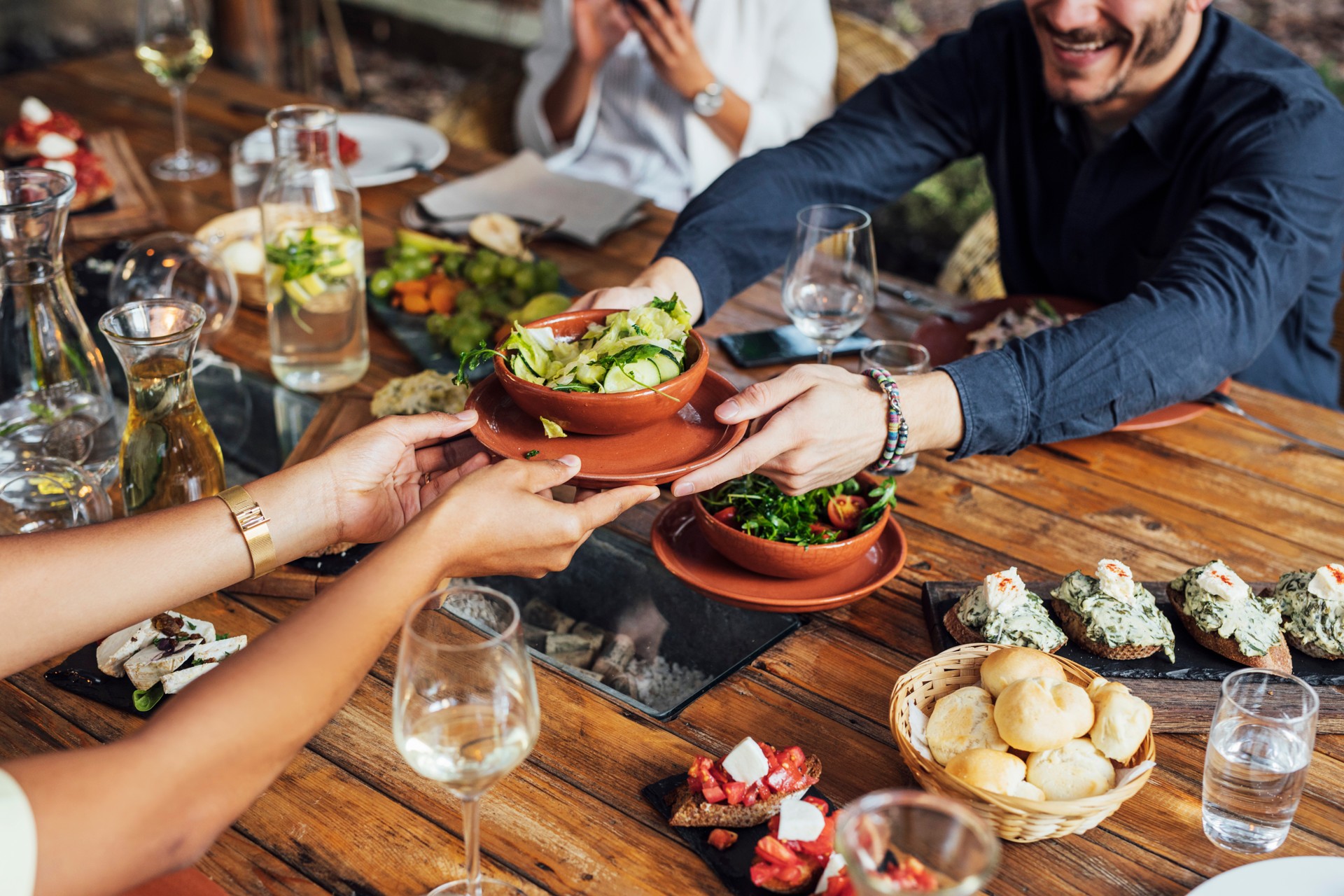 Friends passing a bowl of greens at a shared dinner table
